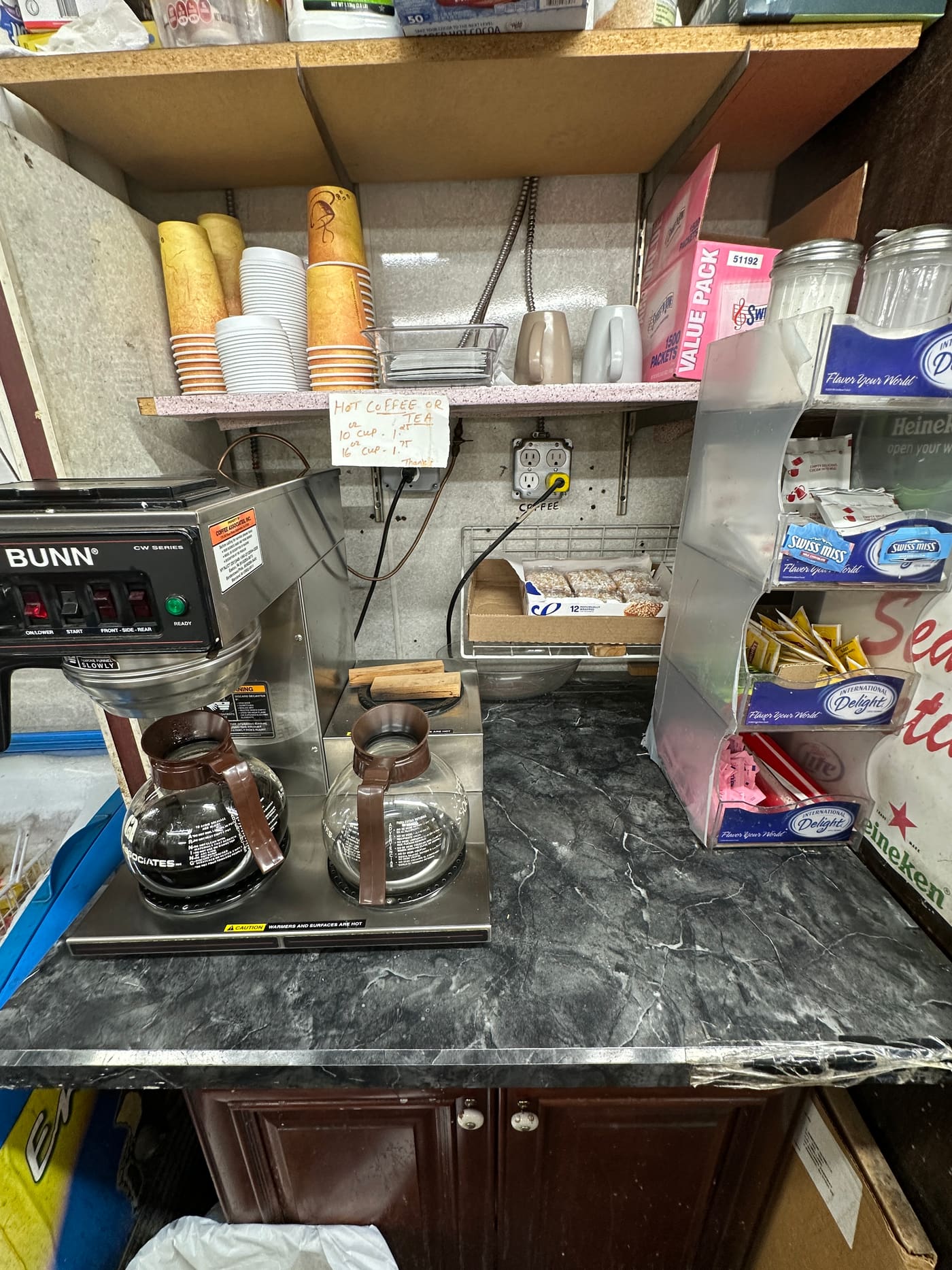 Te-Amo's self-serve coffee station: a BUNN brewer with two fresh pots, stacked cups in two sizes, and a rack of creamers, sugar and stirrers.